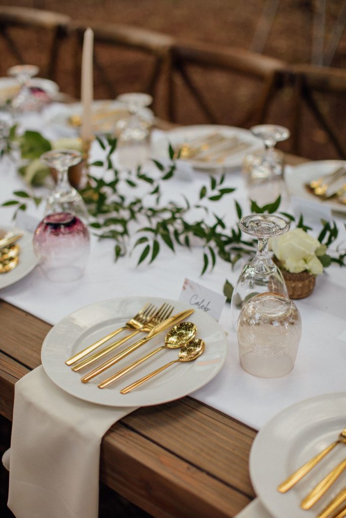 Close up shot of table setting with gold utensils, white plate and wine and water glasses